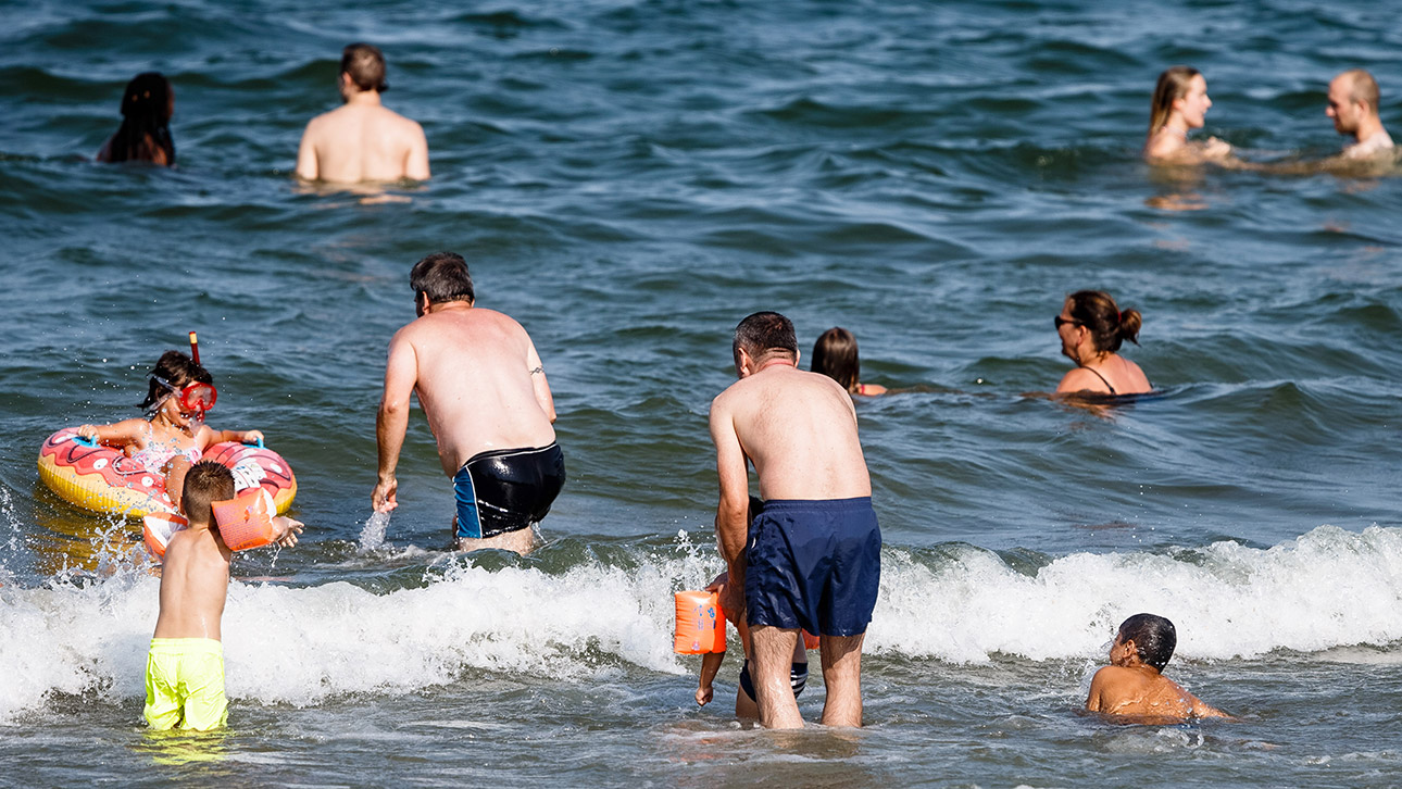 Mehrere Menschen gehen in das Meer und spielen in den Wellen.