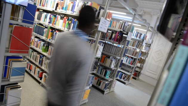 Ein Mann geht an Bücherregalen in einer Bibliothek vorbei.