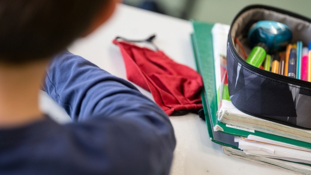 Ein Junge hat auf seinem Schreibtisch neben Schulheften und Federtasche einen Mundschutz liegen.