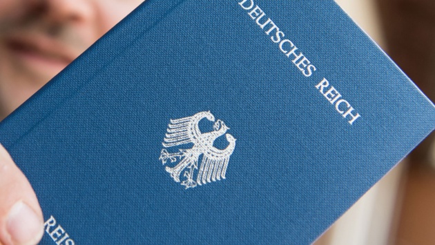 Ein blauer Reisepass wird von einer Hand ins Bild gehalten, auf ihm ist in Goldbuchstaben "Deutsches Reich" vermerkt.