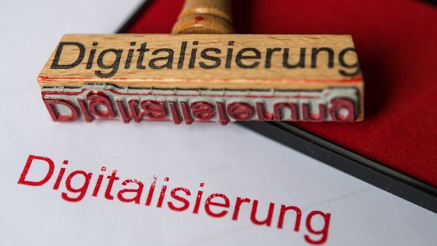 Ein Stempel mit dem Wort „Digitalisierung“ und ein rotes Stempelkissen liegen auf einem Blatt Papier.