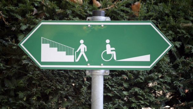 Ein Schild weist darauf hin, dass Fußgänger links eine Treppe und Rollstuhlfahrer rechts eine Auffahrt benutzen können.