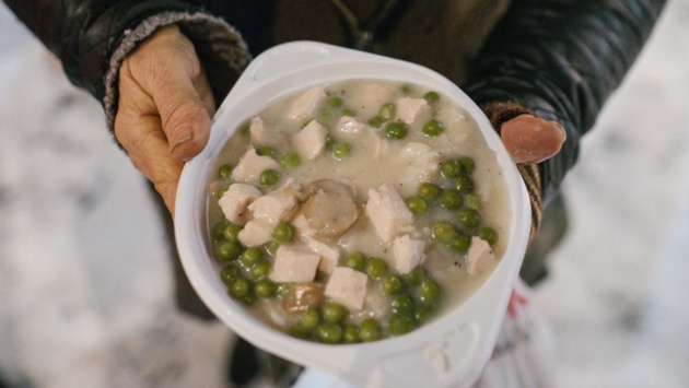 Eine obdachlose Frau hält eine Schüssel mit einer warmen Mahlzeit in den Händen.