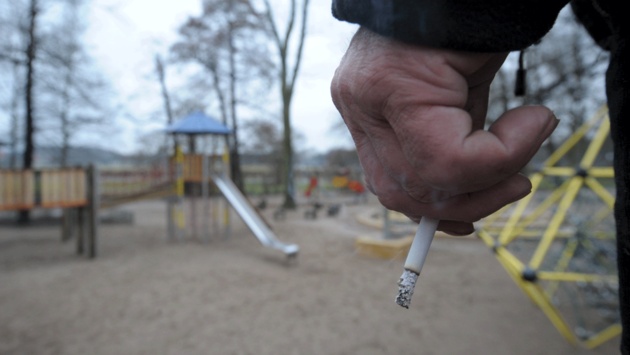 Ein Mann hält auf einem Spielplatz eine Zigarette in der Hand.