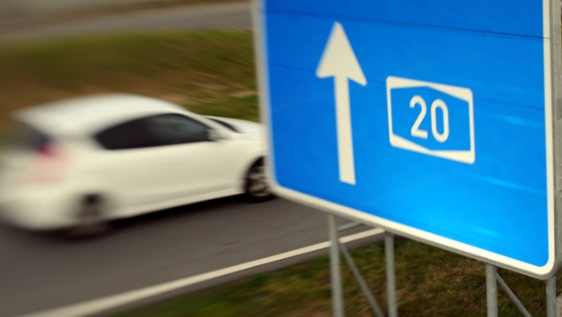 Ein Auto rast an einem Autobahnschild mit einem Pfeil zur A 20 vorbei.