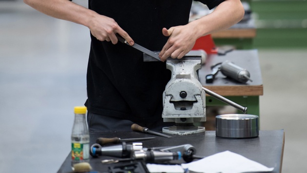 Ein junger Mann arbeitet am Schraubstock in einer Ausbildungswerkstatt für Mechaniker.