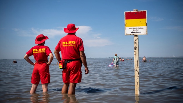 Zwei Mitglieder der DLRG (Deutsche-Lebens-Rettungs-Gesellschaft) stehen im knietiefen Wasser und blicken aufs Meer.